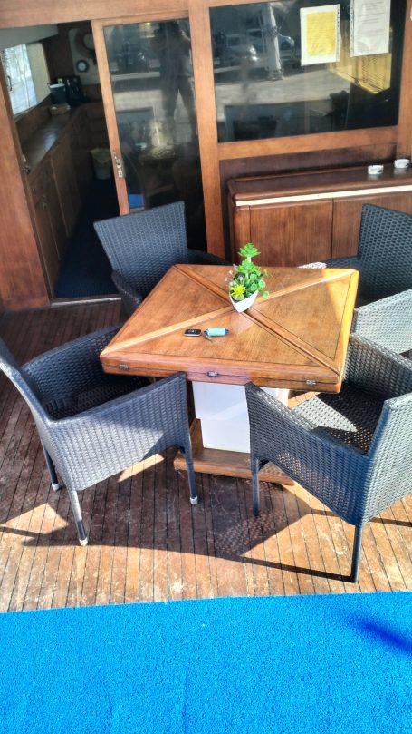 Tavolo quadrato in legno con quattro sedie attorno, pianta decorativa al centro.