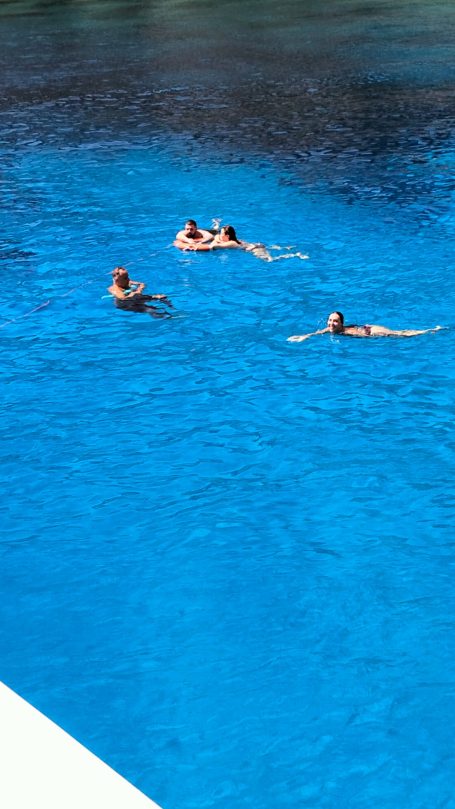 Due persone nuotano in una piscina blu, circondate da acqua limpida.