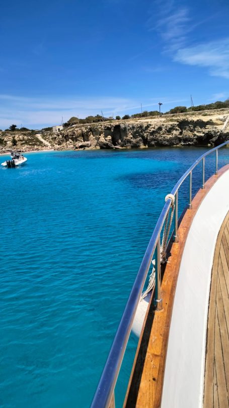 View of a turquoise sea from a boat with rocky shores in the background.