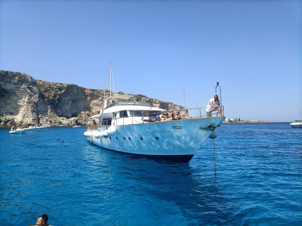 Yacht anchored near rocky cliffs in clear blue waters under a sunny sky.