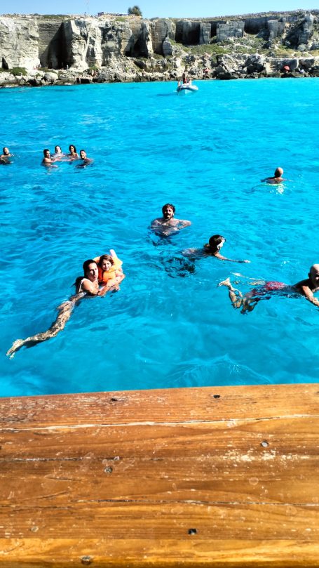 Persone che nuotano in acqua turchese vicino a una riva in legno.