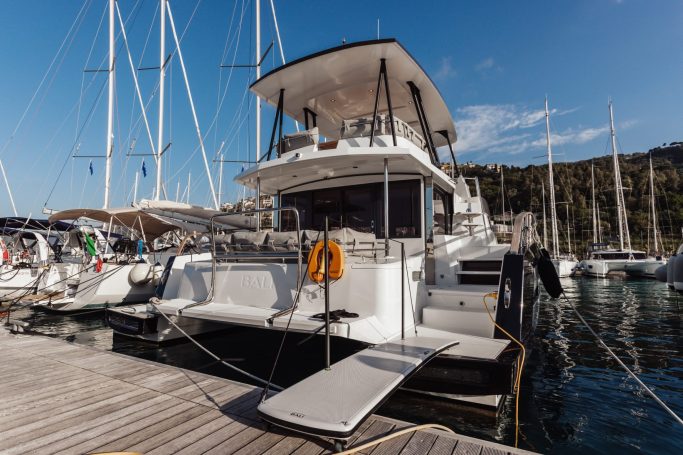 Catamaran docked at a marina, surrounded by sailboats and calm waters.